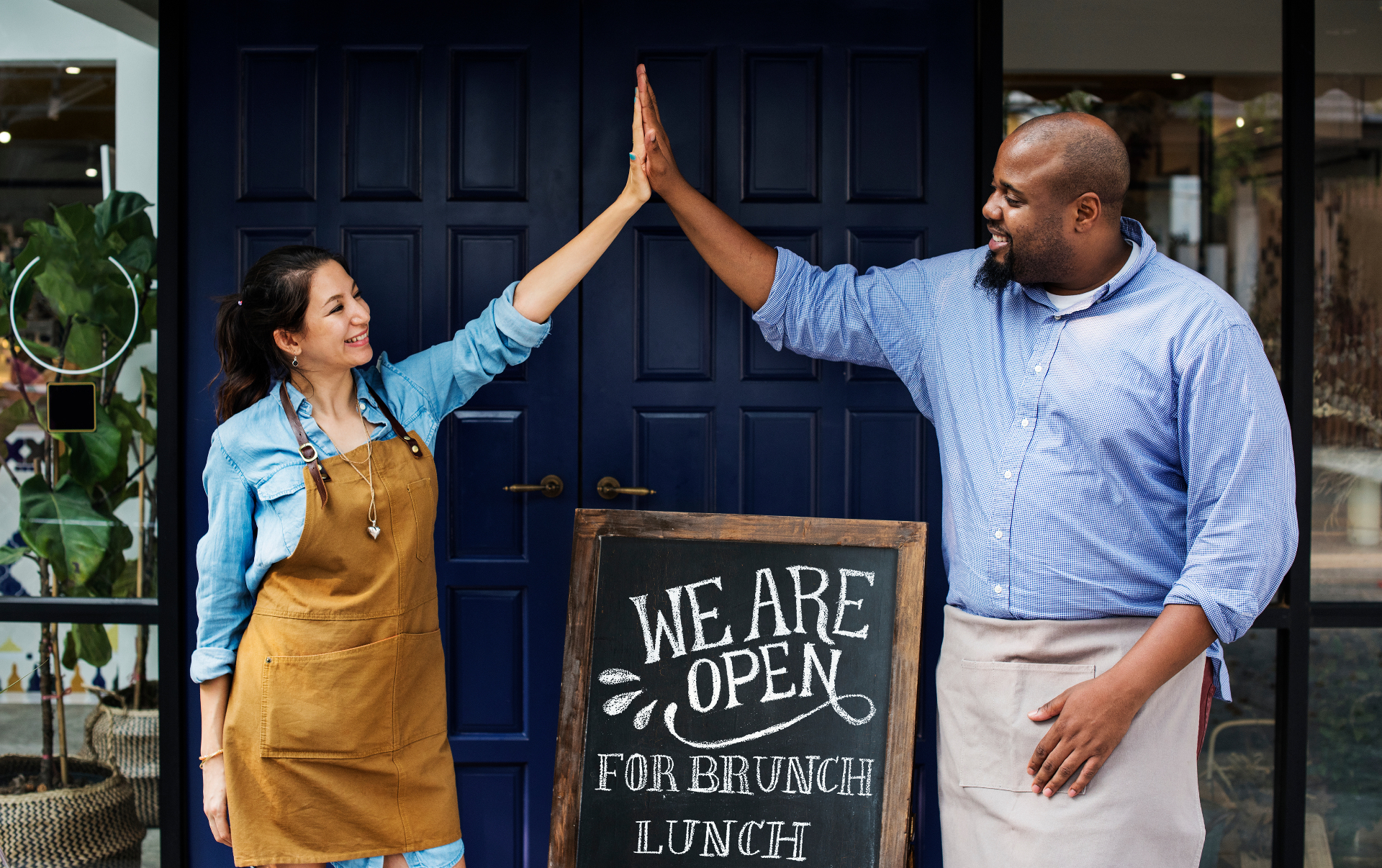 Two small-business owners high-fiving outside their open shop